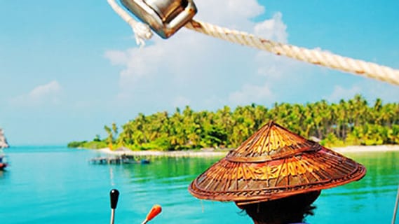 Kapitän am Steuerrad eines Segelboots bei Sonnenschein vor einer Insel bei Koh Samui im Juni